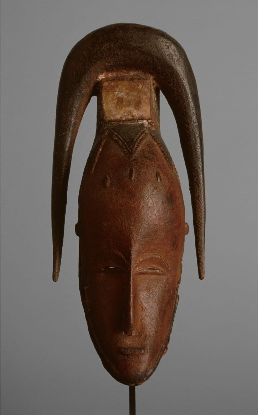 Wooden mask with elongated horns and carved facial features displayed against a plain background.