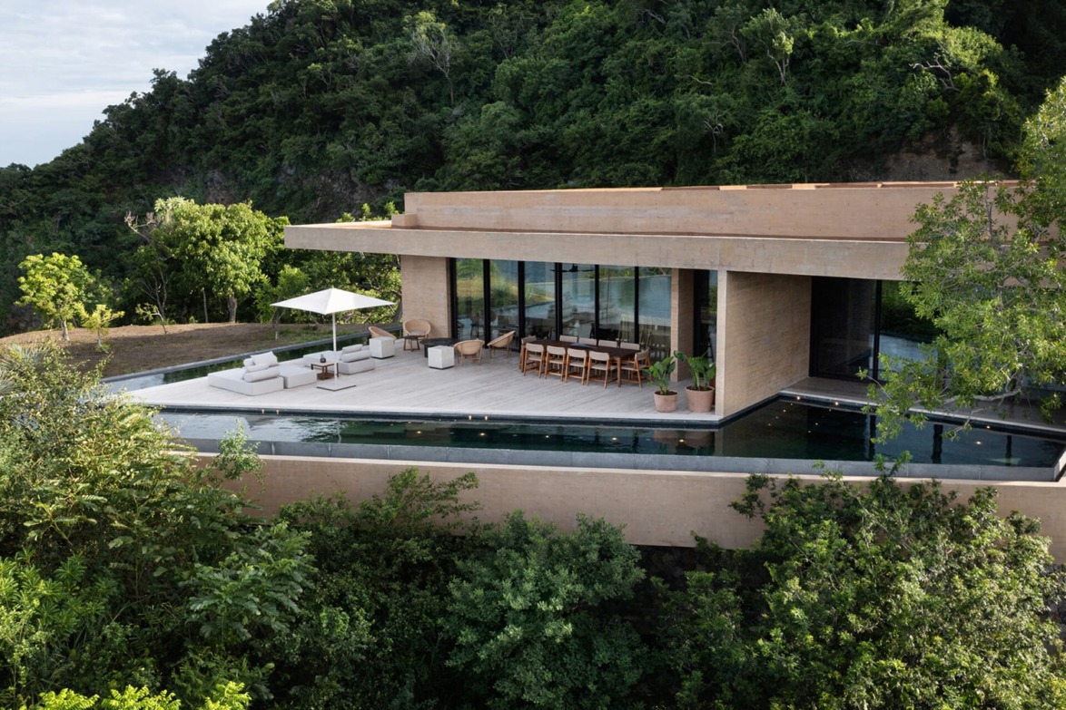 Modern hillside villa with large terrace, outdoor dining area, and an infinity pool surrounded by lush greenery and forest.