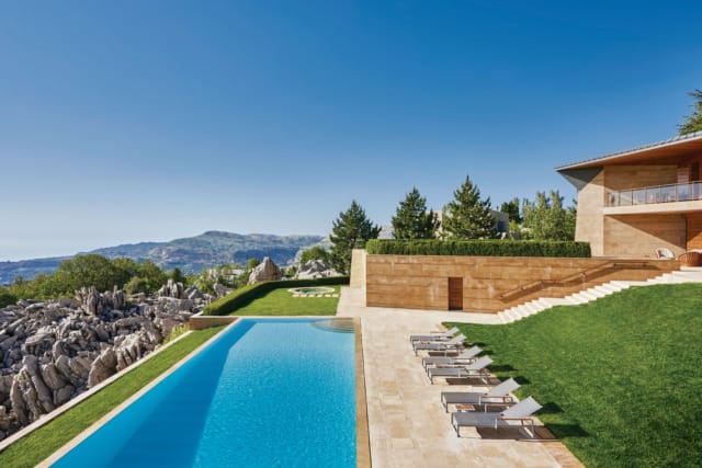 Luxury villa with infinity pool, sun loungers, and mountain view under clear blue sky.