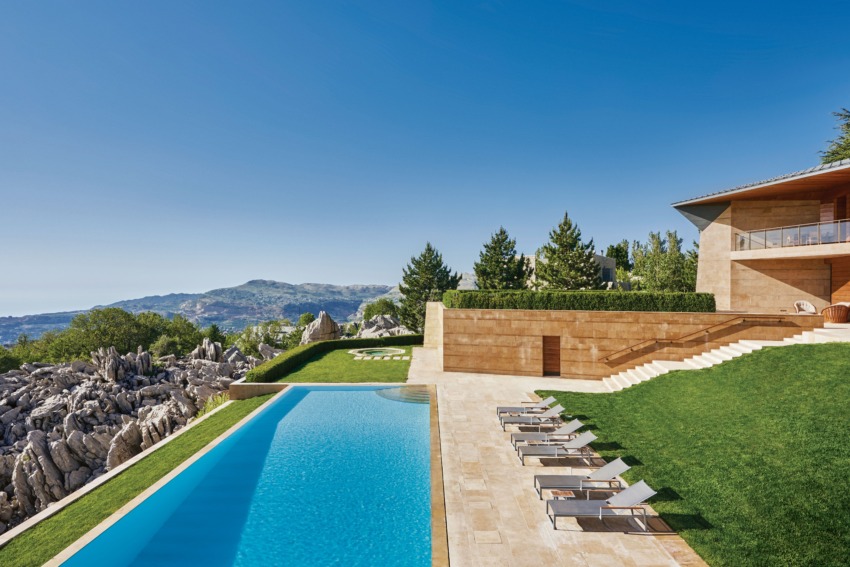 Luxury villa with infinity pool, sun loungers, and mountain view under clear blue sky.