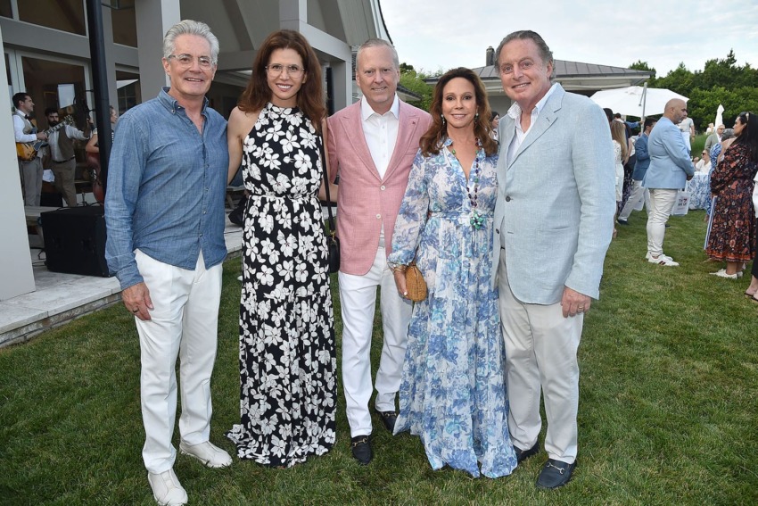 A group of five people dressed in formal attire posing outdoors on grass.