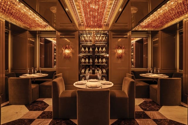 Luxurious restaurant interior with elegant table settings, plush seating, mirrored walls, and warm ambient lighting.
