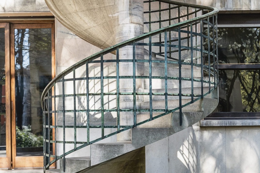 Spiral concrete staircase with metal railing on exterior of a beige building with large windows.