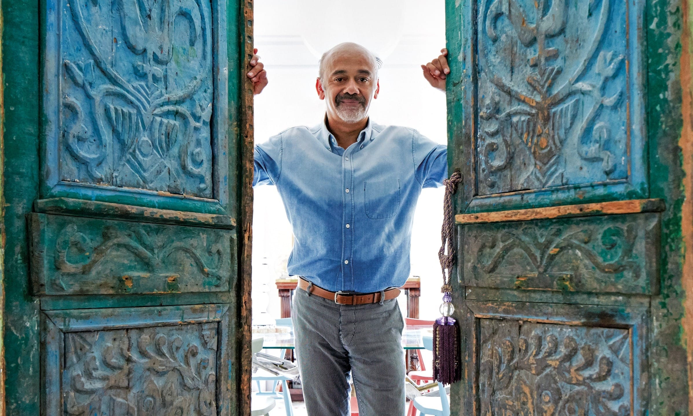 Man wearing a blue shirt, standing between two ornate blue doors with a smile.