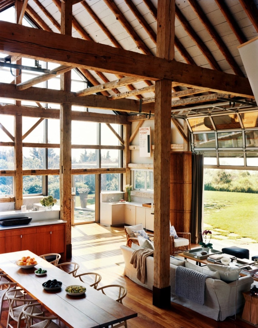 Spacious open-plan living area with exposed wooden beams, large windows, modern furniture, and a view of a garden.