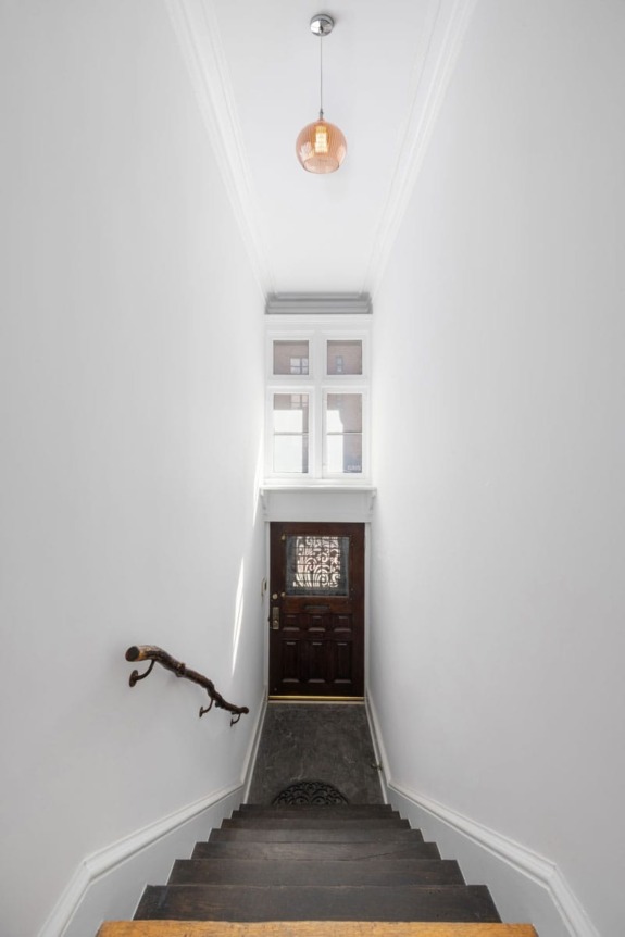 View of a narrow staircase with dark wood steps and a rustic handrail, leading down to a wooden door with a decorative window.