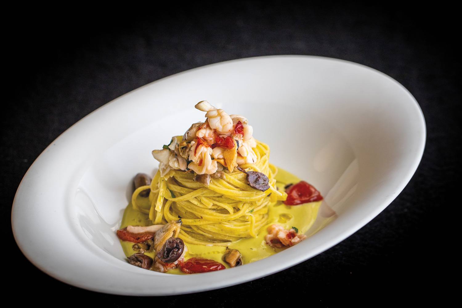 A plate of gourmet pasta topped with seafood, featuring shrimp, mussels, and cherry tomatoes on a creamy sauce.
