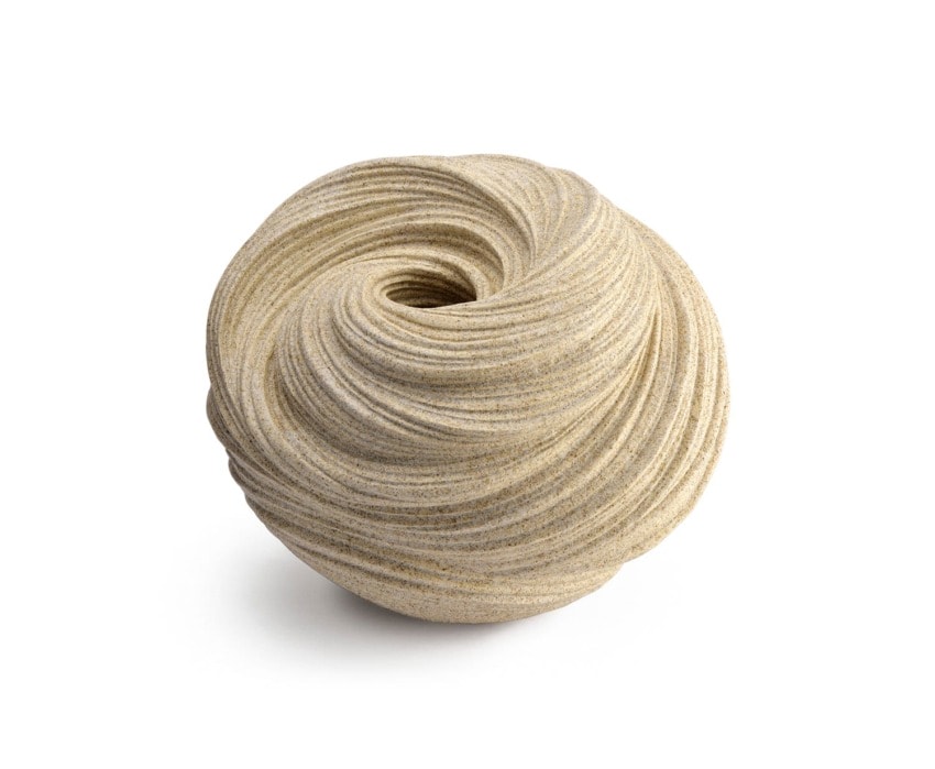 Abstract sand sculpture resembling a coiled swirl with textured, layered patterns against a plain white background.