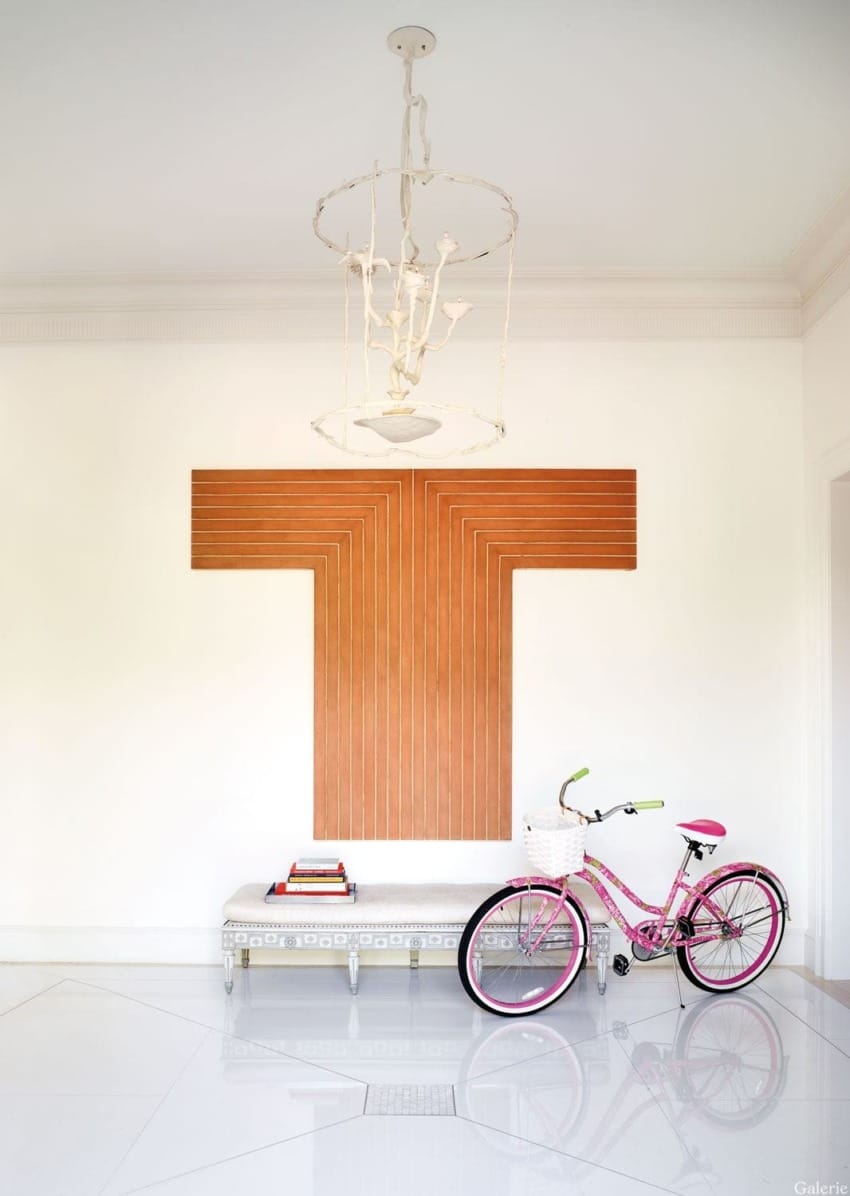 Modern interior with geometric wall art, decorative bench, and pink bicycle in a bright, minimalist room.