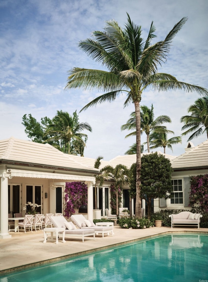 Tropical poolside patio with palm trees, sun loungers, and a cozy seating area outside a luxurious villa under a blue sky.