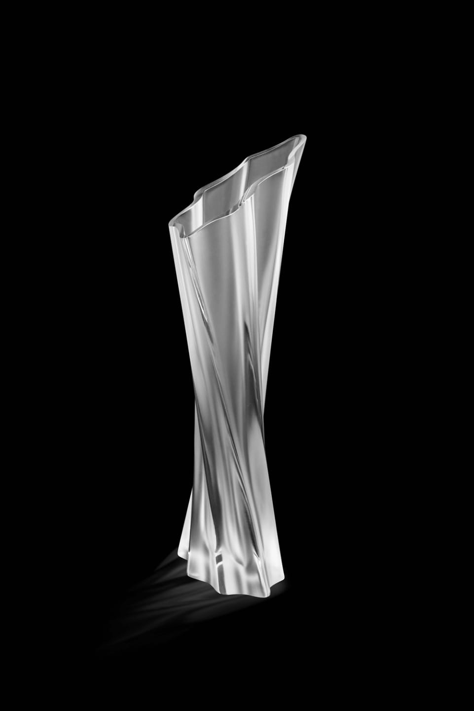 Silver, abstract, twisted sculpture with smooth and reflective surfaces, casting a shadow on a black background.