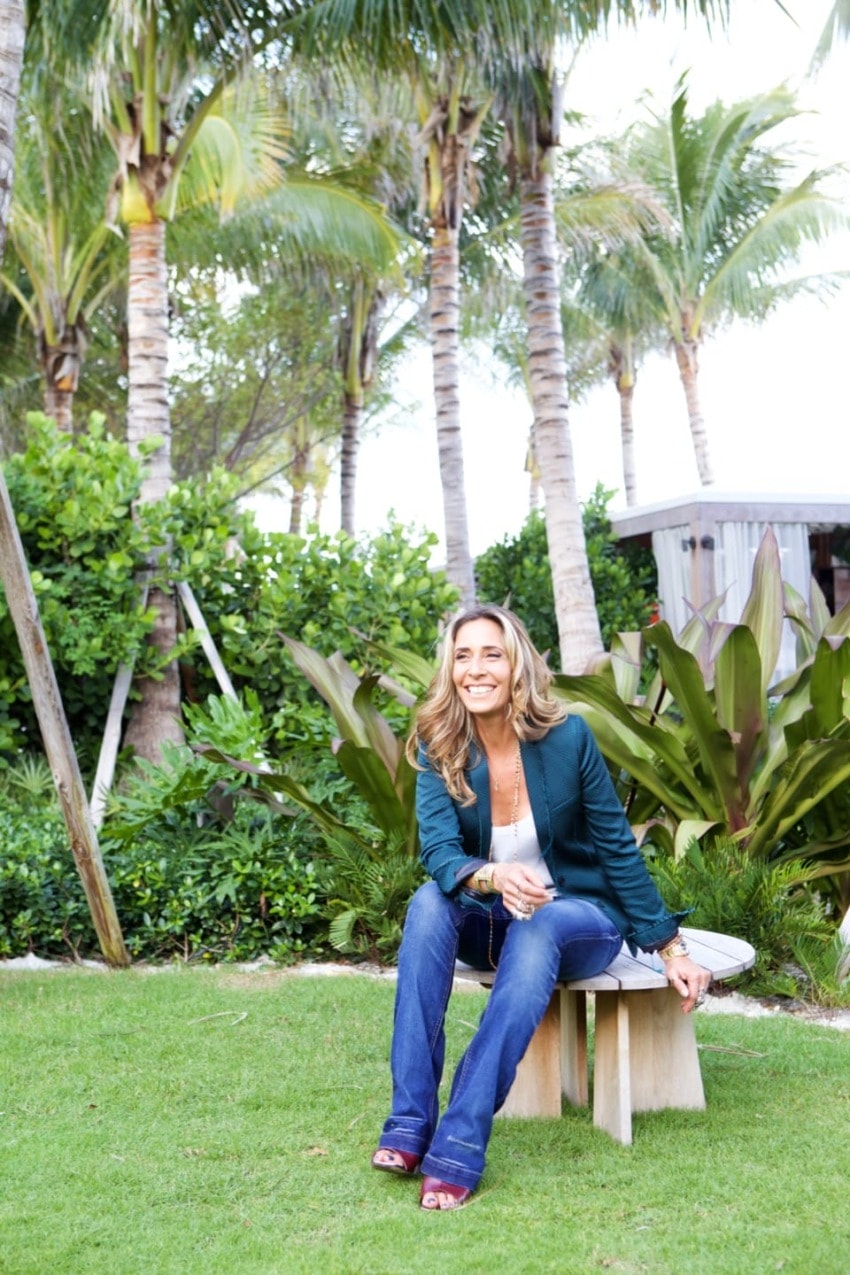 Woman sitting on a bench in a tropical garden with palm trees in the background.