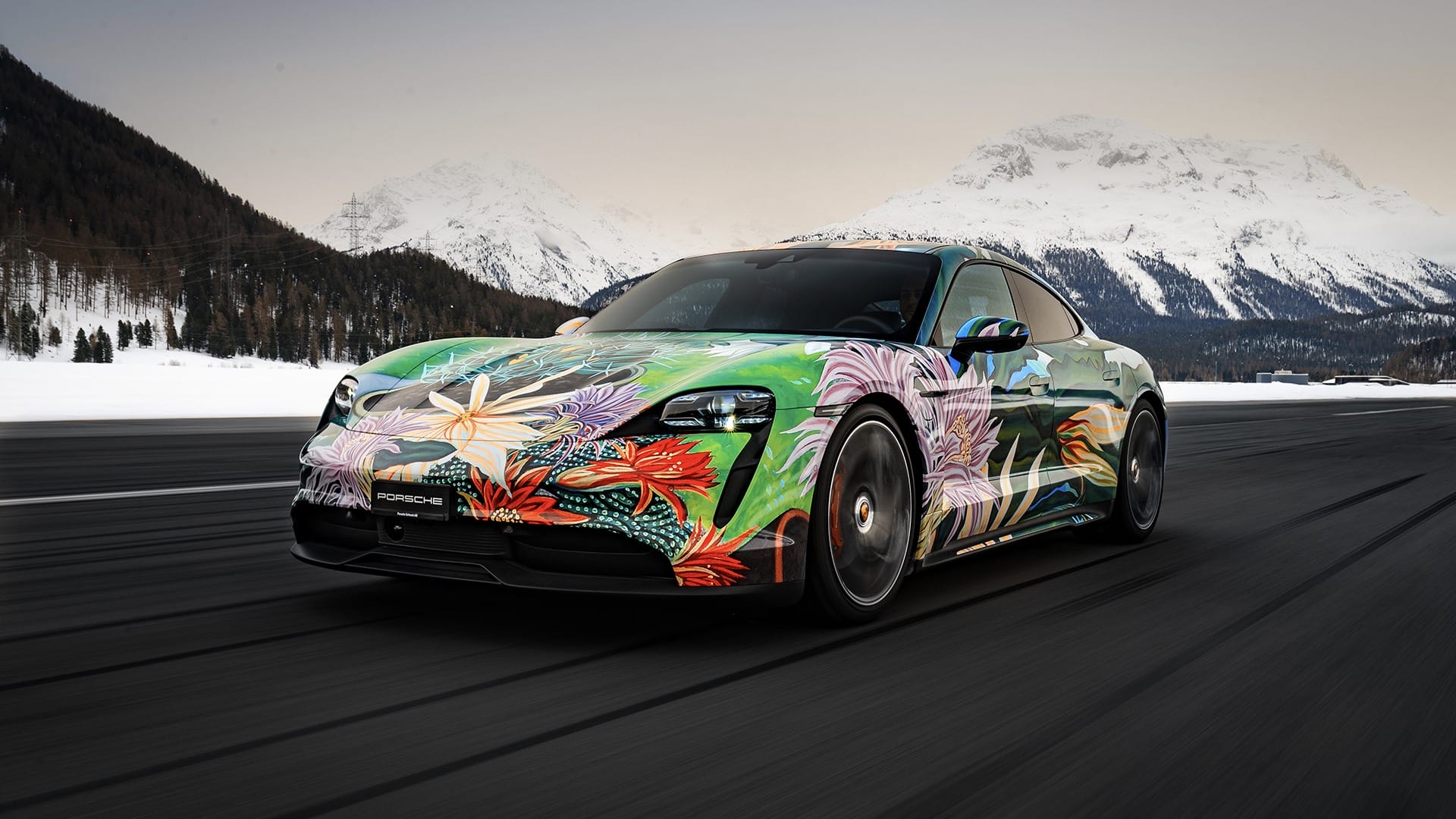 Electric sports car with colorful floral wrap driving on a snowy mountain road.