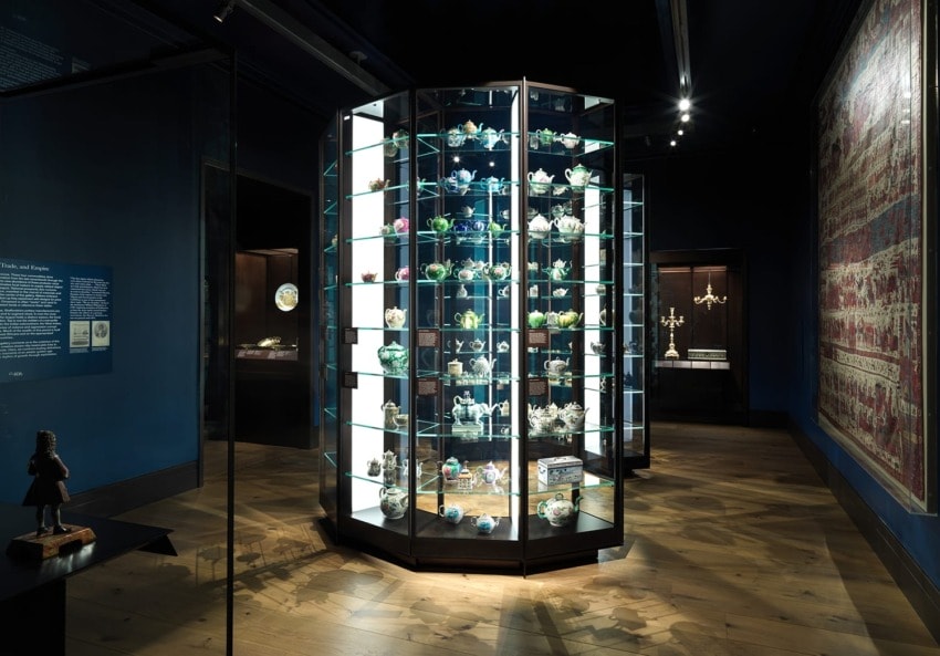 Dimly lit museum room featuring a glass display case filled with assorted decorative artifacts on a wooden floor.