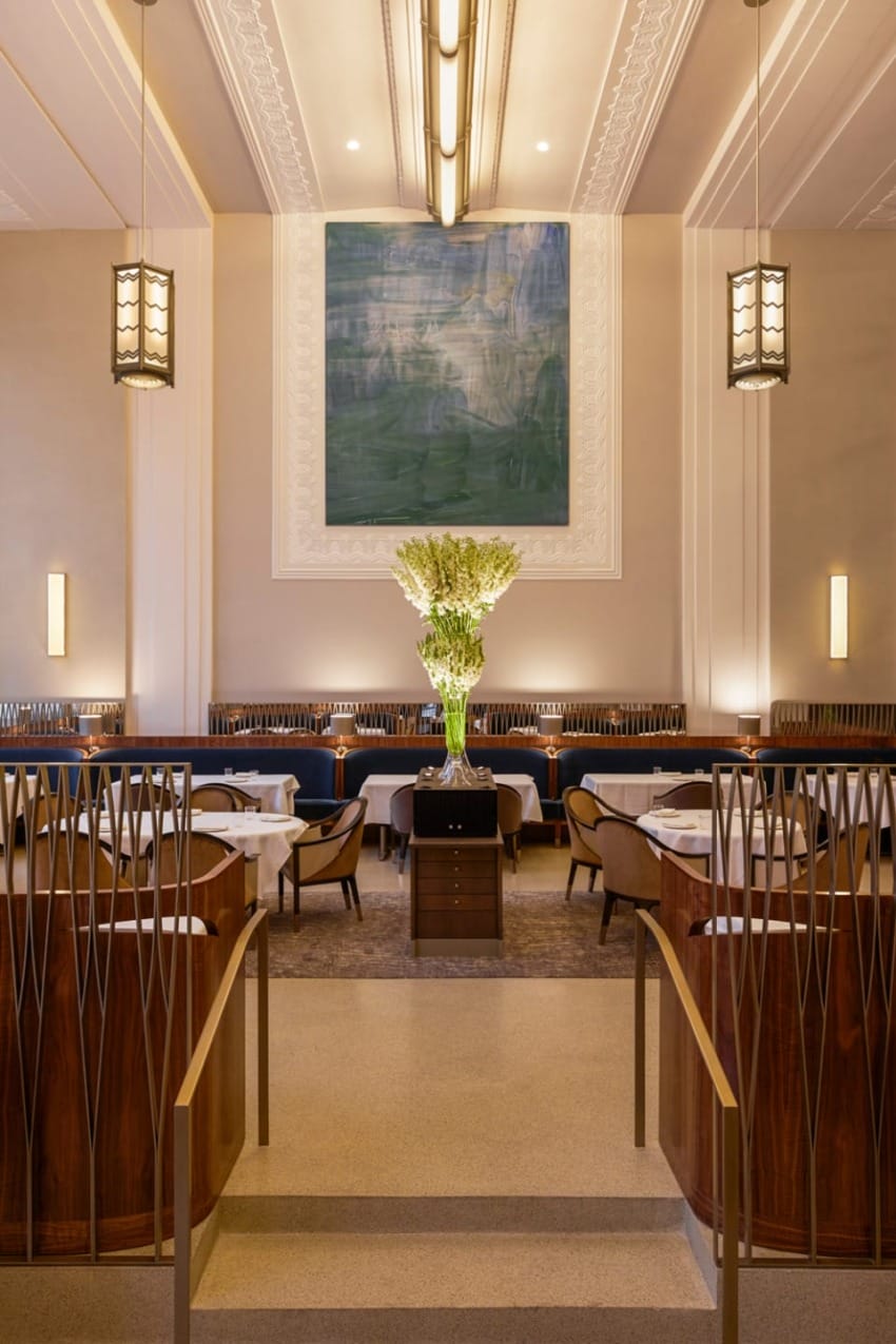 Elegant restaurant interior with tall ceilings, modern lighting, artwork on the wall, and tables neatly arranged for dining.