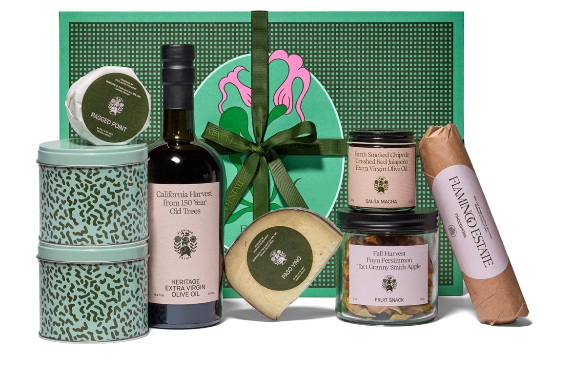 Gift box with olive oil, cheese, honey, spice blend, olives, and a sausage wrapped in paper, all elegantly arranged.