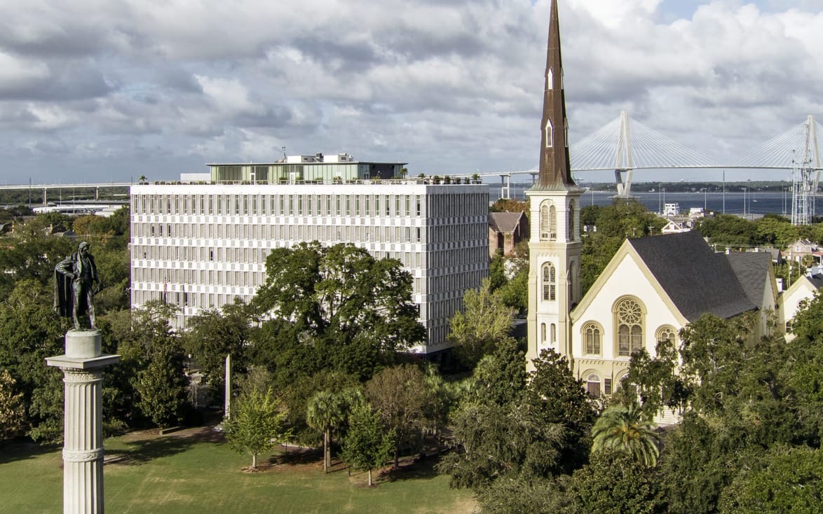 Aerial view of a historic church and monument with a modern bridge in the background under a cloudy sky.