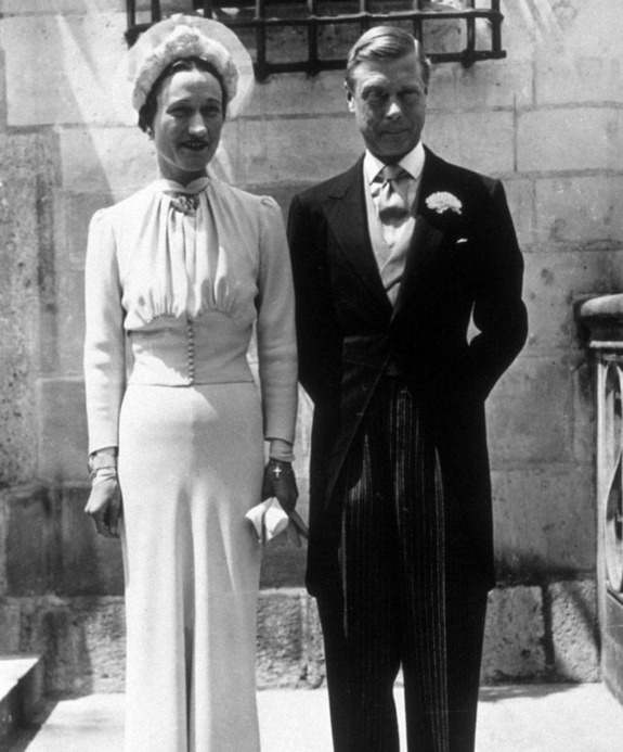 A couple dressed in formal attire, standing side by side in front of a historic building.
