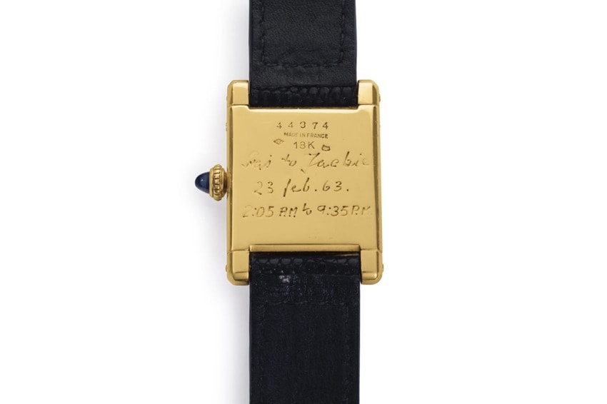 Back of vintage gold wristwatch with black leather strap, engraved details visible on the case.