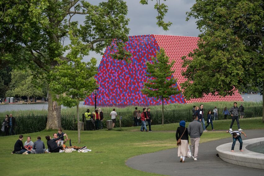 People enjoying a day at the park with a colorful geometric art installation near a pond surrounded by trees.