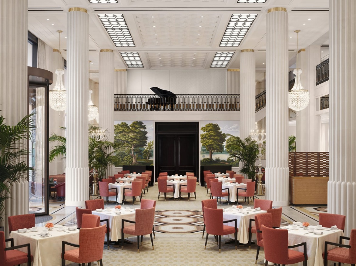 Elegant dining hall with red chairs, white tablecloths, tall columns, chandeliers, and a grand piano on an elevated platform.