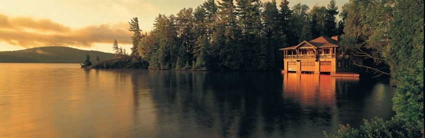 Lakeside cabin surrounded by trees at sunset with calm water reflecting the golden light.