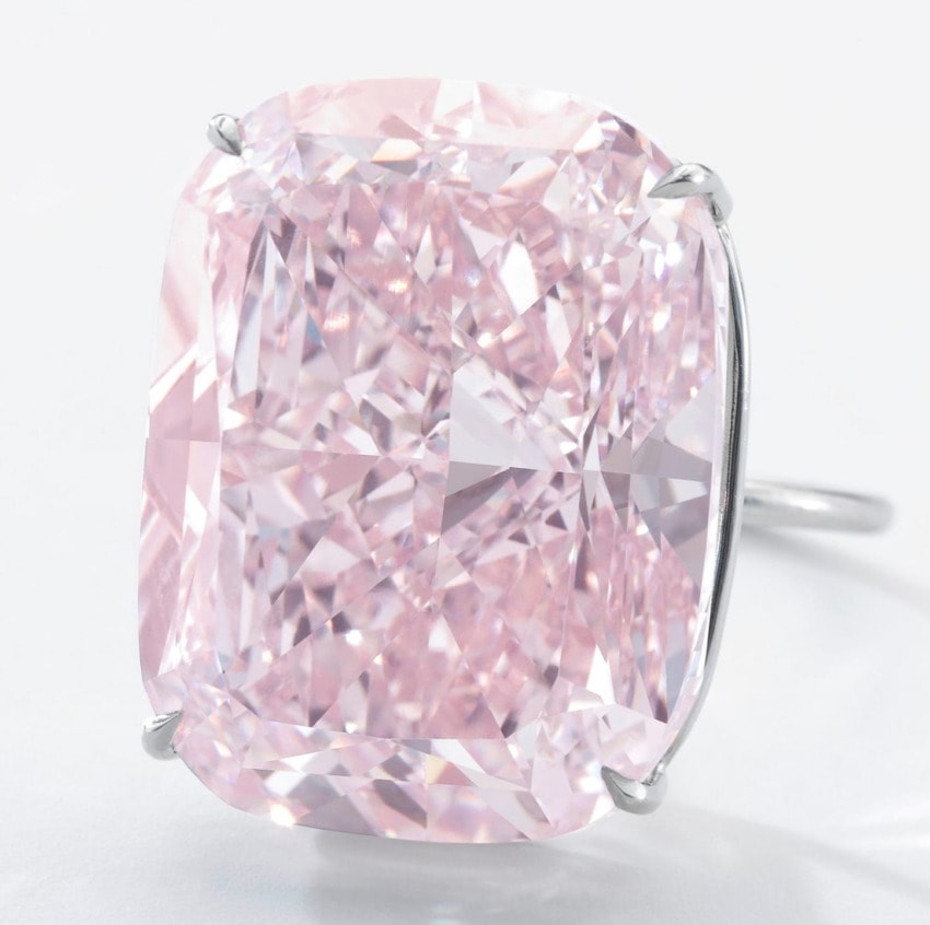 Large pink diamond ring with a cushion cut, set in a simple metal band against a white background.