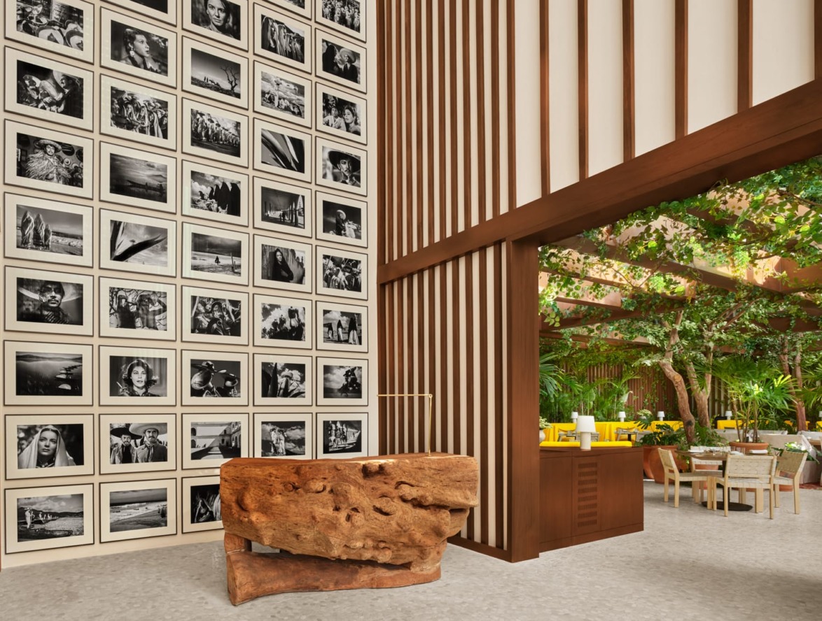 Modern interior with a wall of black and white photos, a stone sculpture, and dining area in a garden setting.