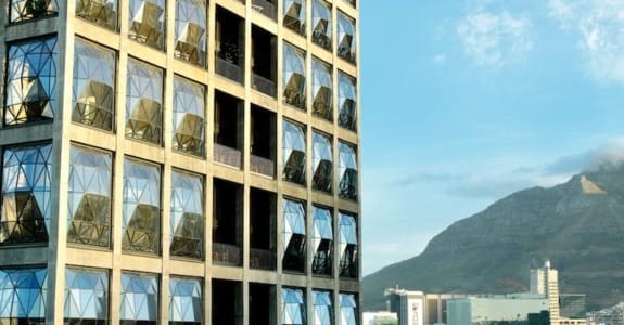 Modern building with geometric windows against a backdrop of mountains and a clear blue sky.