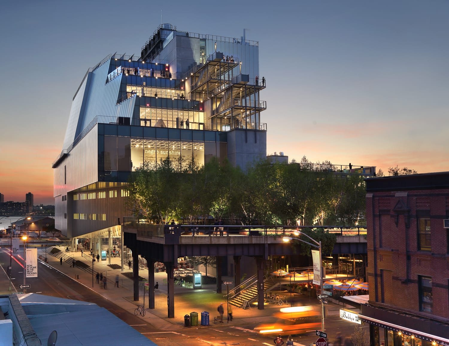 Modern museum building at sunset with illuminated windows and outdoor terraces, located in an urban setting.
