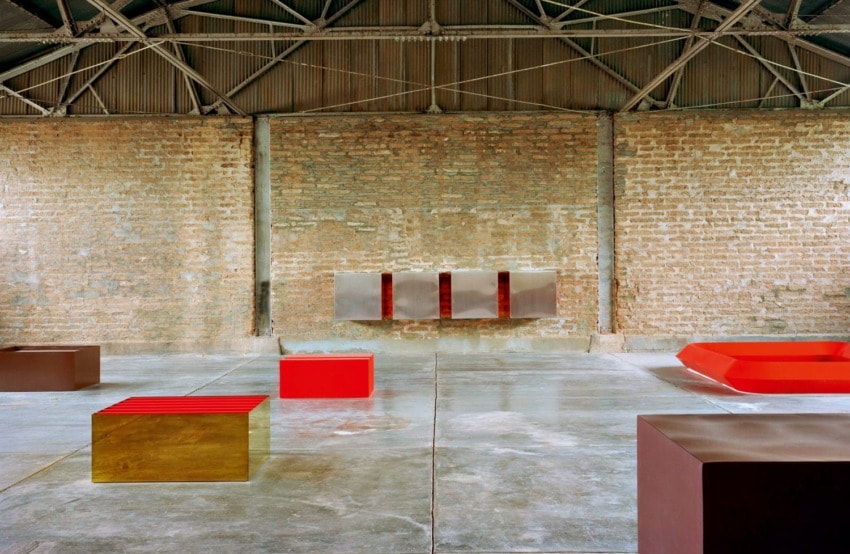 Industrial-style room with exposed brick walls, geometric art pieces in red and brown colors on a polished concrete floor.
