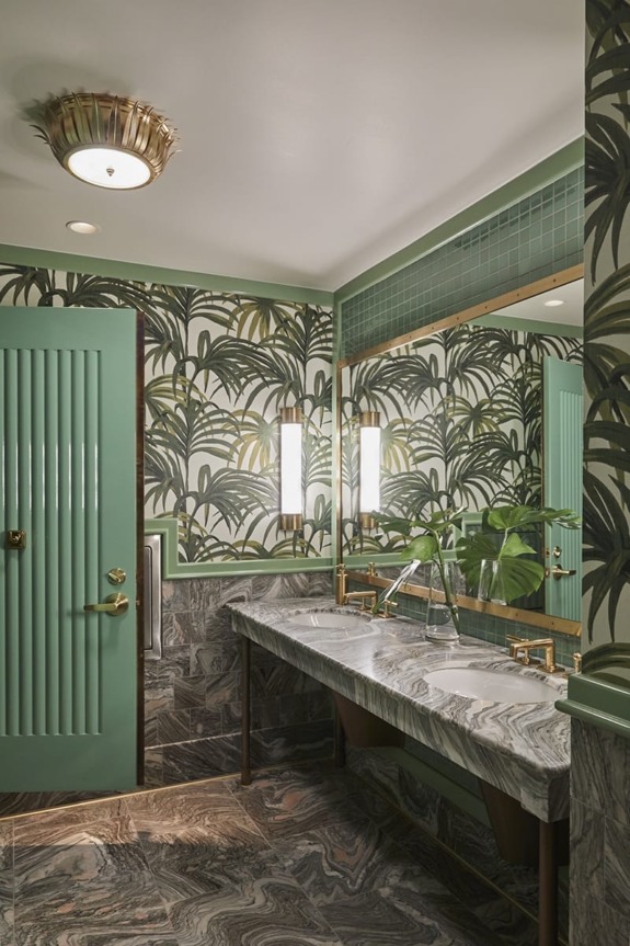 Art deco bathroom with large mirror, green and gold accents, tropical wallpaper, and marble sink.