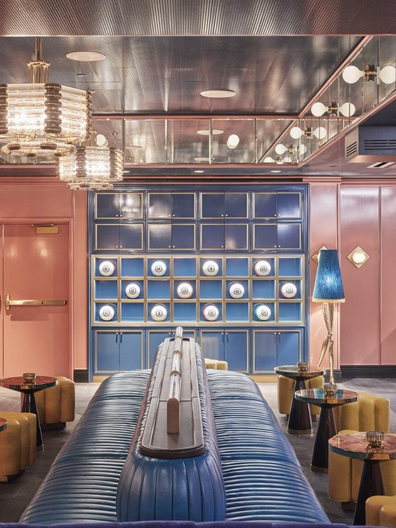 Chic lounge with blue sofas, decorative wall plates, elegant lighting, pink walls, mirrored ceiling, and stylish decor.