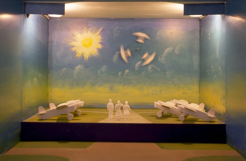 Model airplanes and figures in a display diorama with painted sky and sun background.