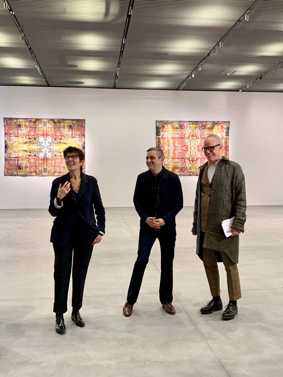 Three people stand in an art gallery with colorful abstract paintings on the walls behind them.