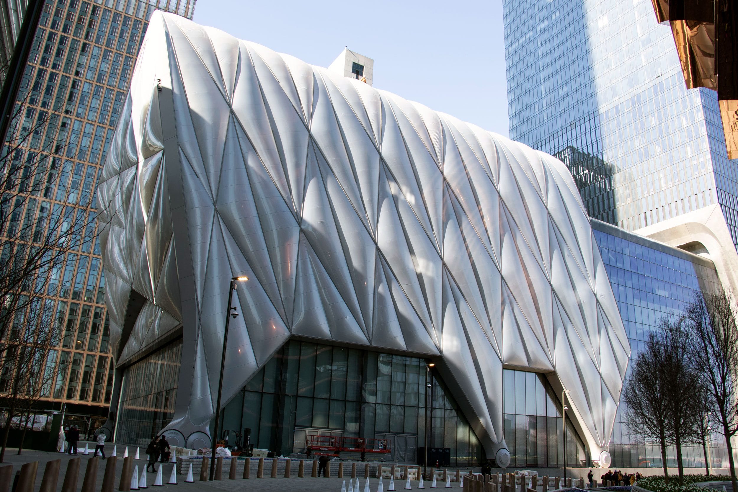 Modern architectural building with a geometric, folded façade in an urban setting, surrounded by tall skyscrapers.