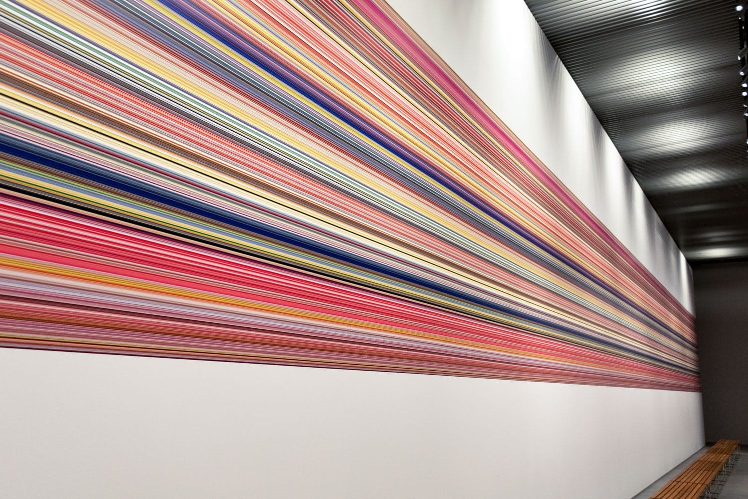 Colorful horizontal stripes on a modern art museum wall, extending across a white space with overhead lighting.