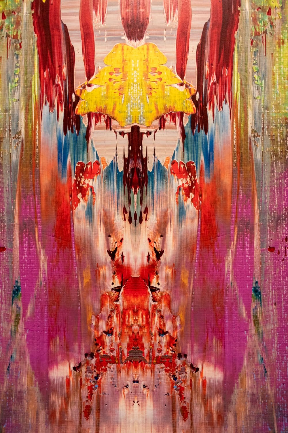 Abstract painting with vibrant colors and symmetrical patterns resembling a waterfall, featuring reds, yellows, and purples.