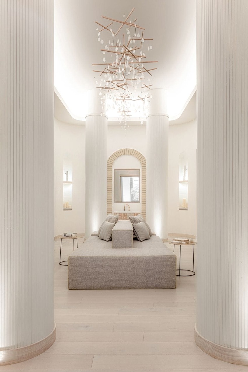 Elegant minimalist bedroom with tall columns, a cozy bed, modern chandelier, and soft lighting, creating a serene atmosphere.