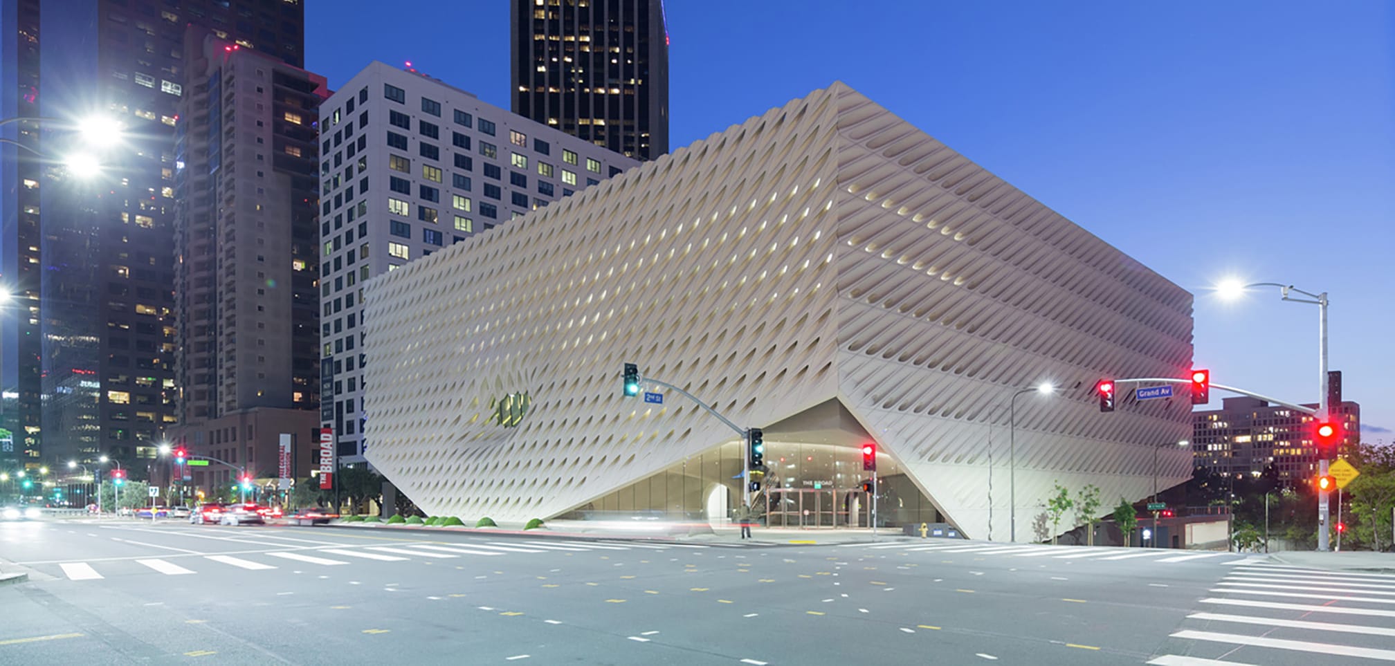 Modern, cube-shaped building with a textured facade, surrounded by city lights and skyscrapers at dusk.