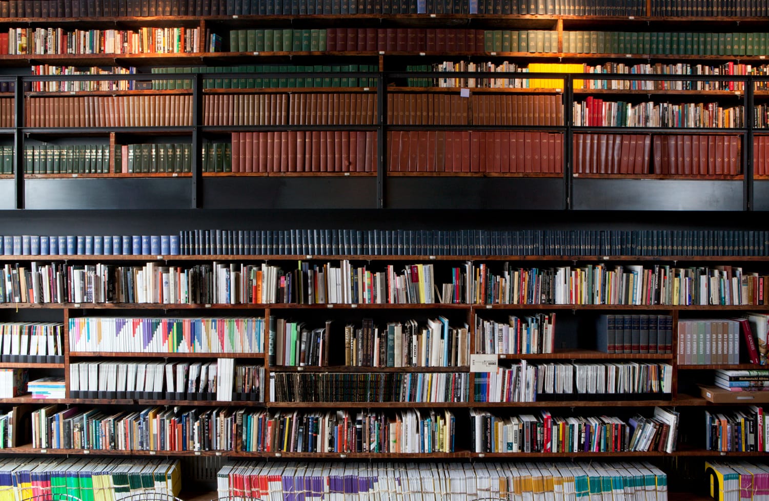 Bookshelves filled with a variety of books organized by size and color in a dimly lit library setting.