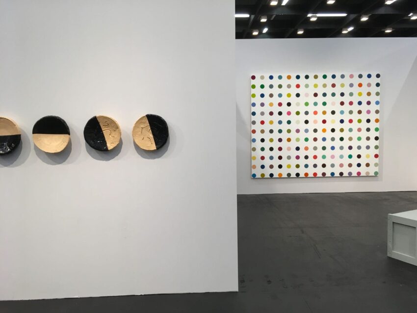 Art gallery with three circular sculptures on left and large colorful polka dot painting on the right wall.