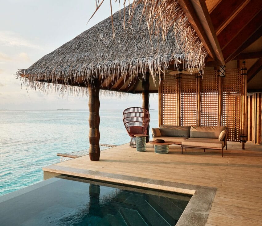 Tropical overwater villa with thatched roof, wooden deck, infinity pool, and ocean view at sunset