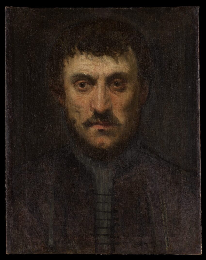 Portrait of a bearded man with short hair wearing a dark coat, set against a dimly lit background