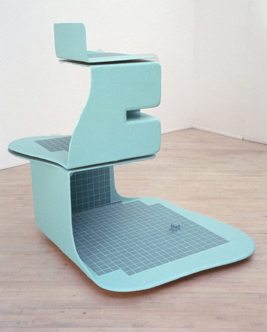 Abstract blue-green sculpture with geometric shapes and grid pattern, placed on a wooden floor in a minimalist room.
