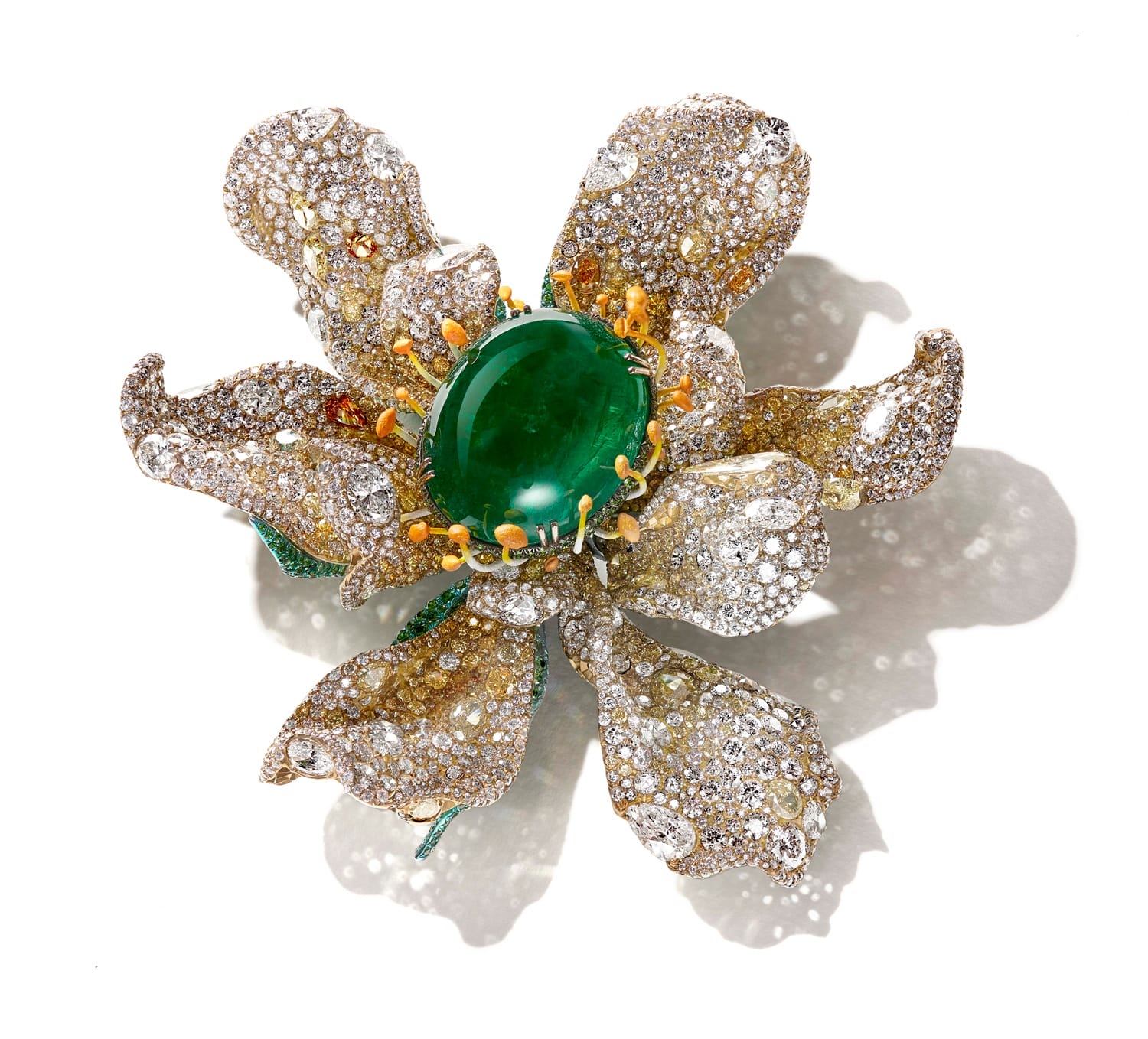 Diamond and emerald flower-shaped brooch with intricate petal details set against a white background.