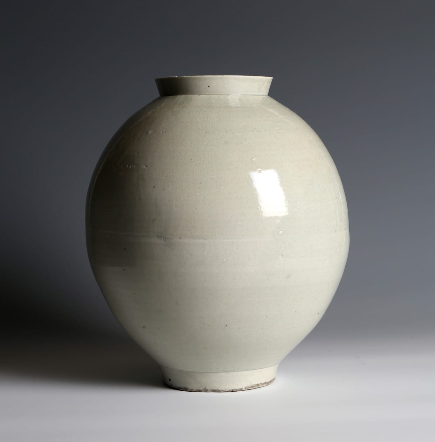 White ceramic moon jar with a glossy finish, placed against a neutral gray background.