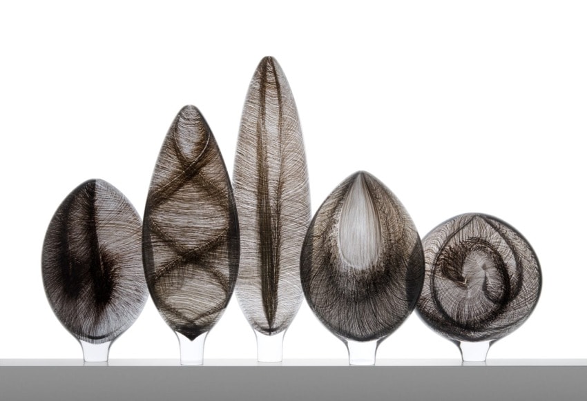 Five glass sculptures with intricate, swirling black and white patterns, displayed in a row against a white background.