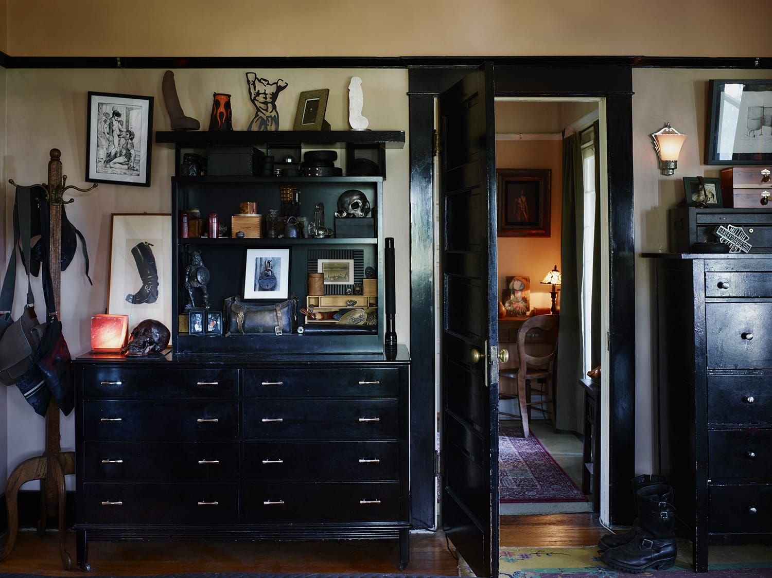 Eclectic room interior with black dresser, shelves filled with various objects, and partially open door leading to another room.