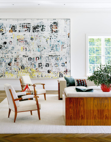 Modern living room with abstract art, wooden chairs, a large sofa, red vase with greenery, and parquet flooring.